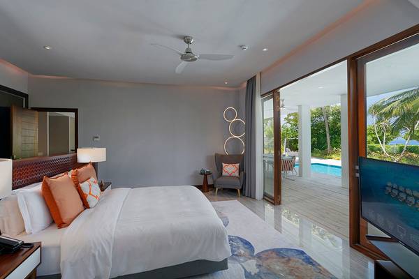 Innenansicht eines Schlafzimmers im Dhigali Maldives Hotel mit Bett, Kissen, Fernseher und Terrasse.