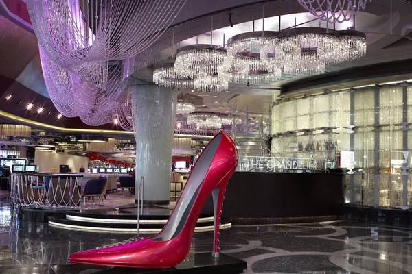 Hotellobby mit einer großen roten High-Heel-Skulptur, Kristallkronleuchtern und einer Bar.