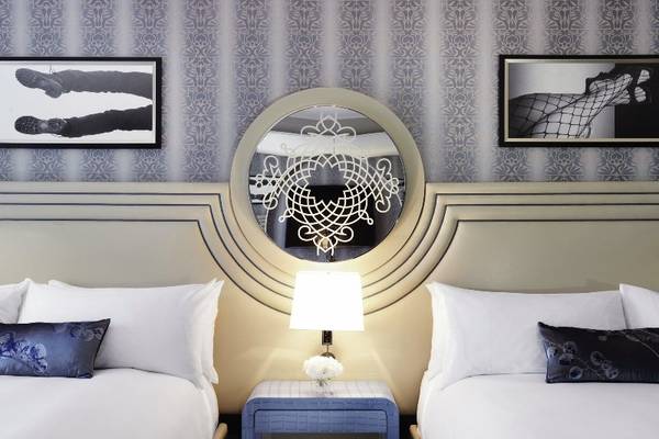 Doppelbett im Hotelzimmer des Cosmopolitan von Las Vegas mit gemusterten Wänden, einem runden Spiegel und einem Nachttisch.