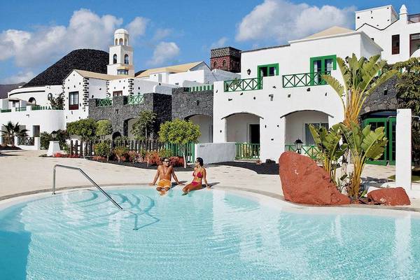 Zwei Gaeste sitzen im Pool des LIVVO Volcan Lanzarote Hotels vor weissen Gebaeuden.