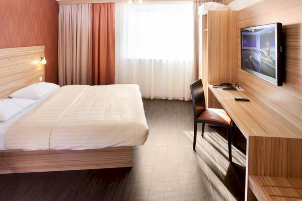 Innenansicht eines Zimmers im Star Inn Hotel Wien Schönbrunn mit einem Bett, Schreibtisch und Fernseher.