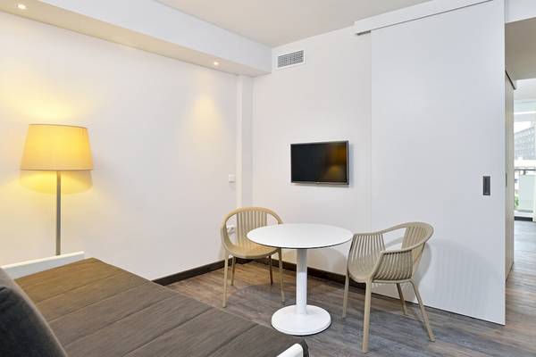 Ein modernes Hotelzimmer von Sol Principe mit weißem Tisch, Stühlen und Fernseher an der Wand.