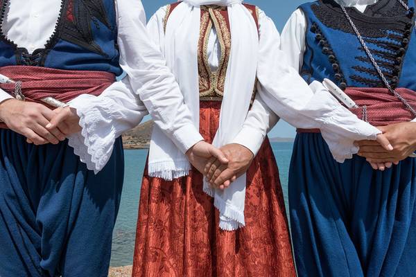 Drei Leute in traditioneller Kleidung stehen am Strand und halten die Hände.