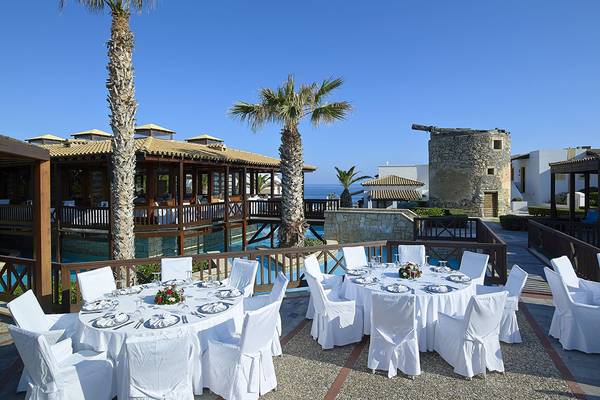Außenbereich des Aldemar Knossos Royal Resort Hotels mit gedeckten Tischen und Stühlen vor dem Pool.