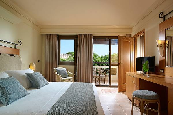 Hotelzimmer im Aldemar Knossos Royal Resort mit Bett, Stühlen, Fernseher und Balkon.