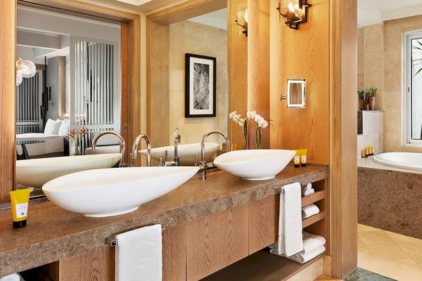 Badezimmer im Shangri-La Le Touessrok Hotel mit zwei Waschbecken, Badewanne und Fenster mit Palmbaumblick.