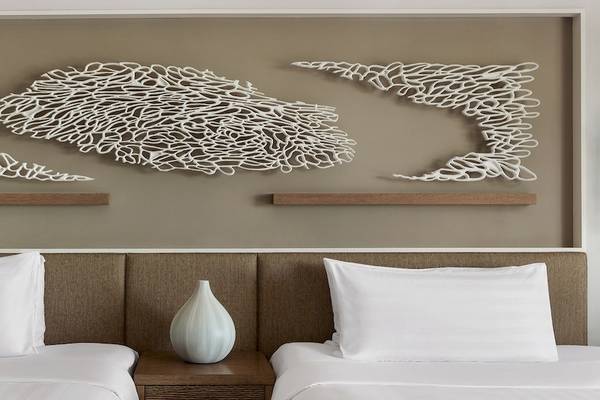Doppelbettzimmer im Shangri-La Le Touessrok Hotel mit drei weißen Wandreliefs und einer weißen Vase auf dem Nachttisch.