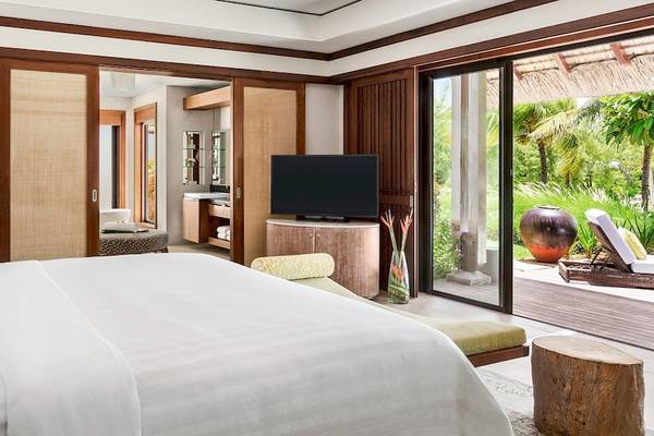 Schlafzimmer im Shangri-La Le Touessrok Hotel mit großem Bett, Fernseher und Glastür, die auf Terrasse führt.