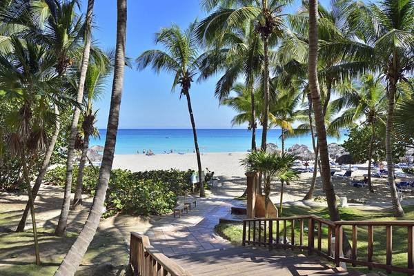 Strandansicht des Melia Las Americas Hotels mit Palmen und Sonnenliegen.