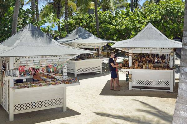 Drei weiße Verkaufsbuden am Strand, zwei Personen stehen vor einer Bude, eine Person sitzt in einer Bude.