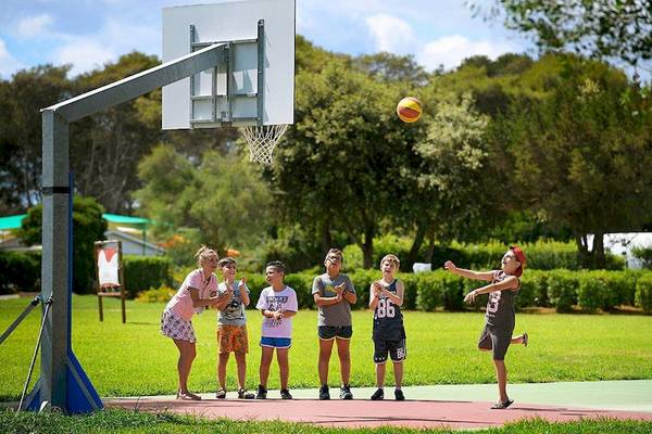Kinder spielen Basketball am VOI Alimini Resort während eine Frau den Ball wirft.