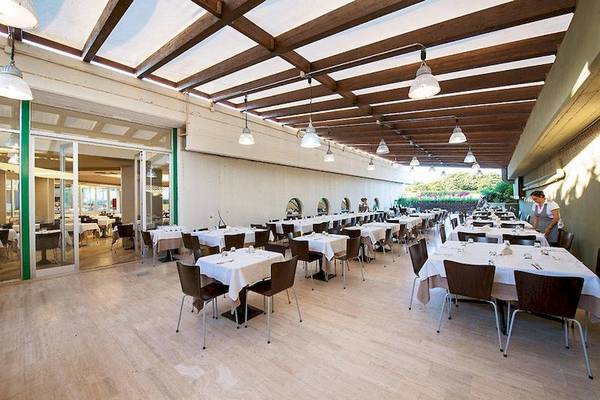 Innenansicht des Restaurants im VOI Alimini Resort mit vielen gedeckten Tischen und einer Angestellten