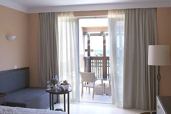 Hotelzimmer des Atlantica Belvedere Resort mit Balkon, Bett, Sessel und Fernseher.