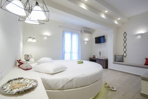 Schlafzimmer im Alkyoni Beach Hotel mit rundem Bett, weißen Kissen und Dekor.