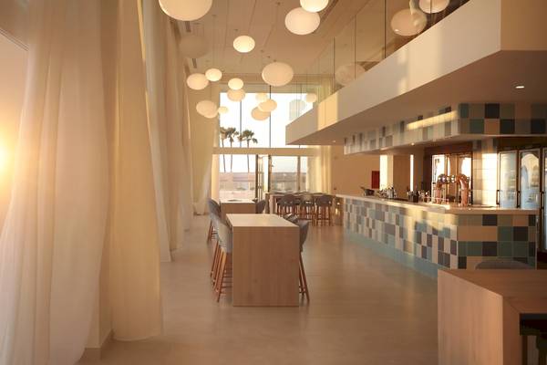 Innenansicht des Iberostar Selection Sabila Hotels mit Bar, Tischen und Stühlen bei Sonnenaufgang.