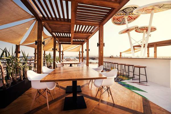 Terrasse des Pyramisa Beach Resort Sahl Hasheesh mit Holztischen, Stühlen und einer Theke.