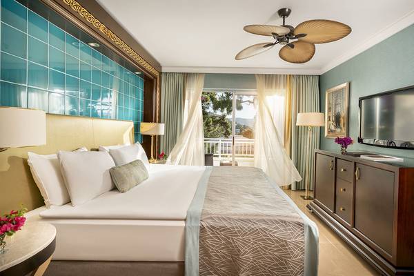 Schlafzimmer im Rixos Premium Bodrum mit blauen Wandfliesen, Bett, Tisch, Fernseher und Deckenventilator.