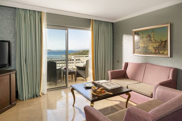 Wohnbereich mit Meerblick im Rixos Premium Bodrum, mit Möbeln, Fernseher und offenem Balkon.