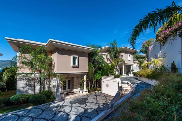 Außenansicht der Rixos Premium Bodrum Villas mit gepflastertem Eingang und tropischer Gartenanlage.