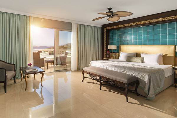 Luxuriöses Schlafzimmer im Rixos Premium Bodrum mit Bett, Bank, Tisch und Balkon.
