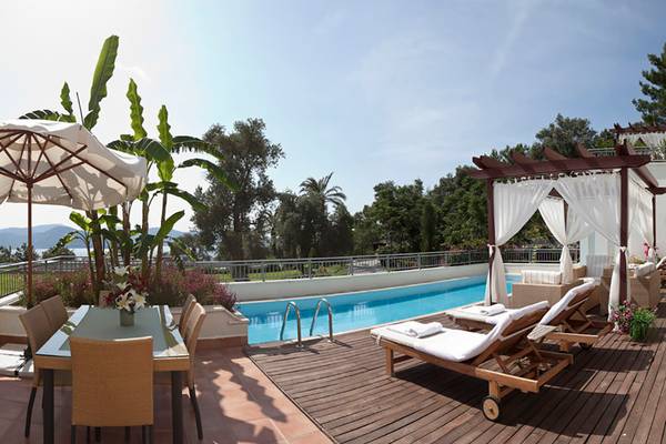Außenpoolterrasse des Rixos Premium Bodrum mit Liegestühlen, Tisch und Sonnenschirm.