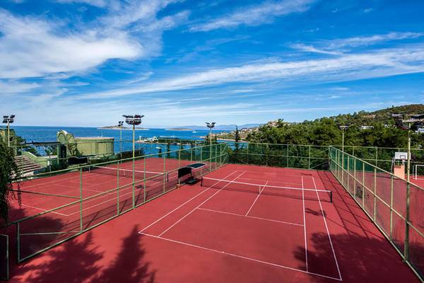 Tennisplatz im Rixos Premium Bodrum mit Blick auf das Meer und eine grüne Umzäunung.