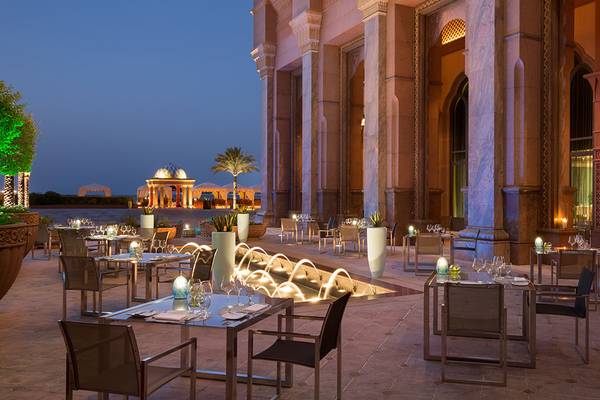 Außenbereich des Emirates Palace Mandarin Oriental Hotel bei Nacht mit illuminierten Säulen und Tischen.