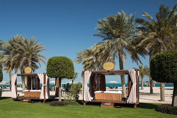Zwei Loungebetten im Freien neben Palmen und einem Meer im Hintergrund, Emirates Palace Mandarin Oriental.