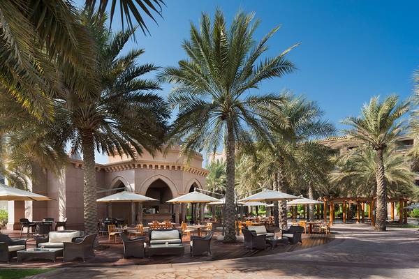 Außenbereich des Emirates Palace Mandarin Oriental Hotels mit Palmen, Tischen und Stühlen.
