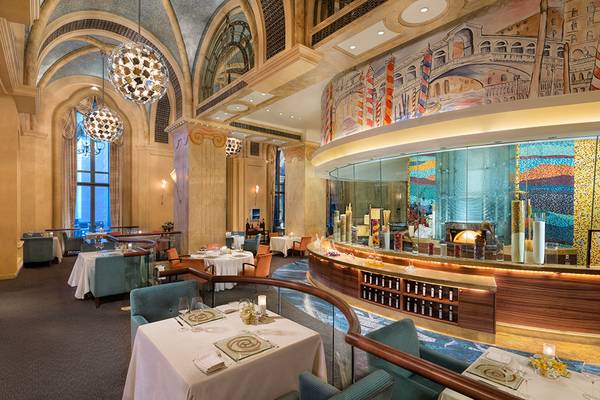 Innenansicht des Restaurants im Emirates Palace Mandarin Oriental mit runden Tischen, Kronleuchtern und einer thematischen Wand.