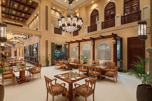 Innenansicht des Restaurants im Emirates Palace Mandarin Oriental mit runden Tischen, Stühlen, Kronleuchtern und Pflanzen.