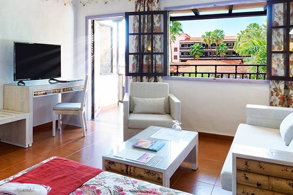 Innenansicht eines Hotelzimmers mit Schreibtisch, Fernseher, Bett, Sofa und Balkon mit Ausblick.