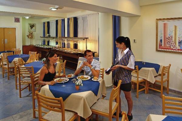 Im Okeanos Beach Hotel sitzen Gäste an einem Tisch und werden von einer Kellnerin bedient.