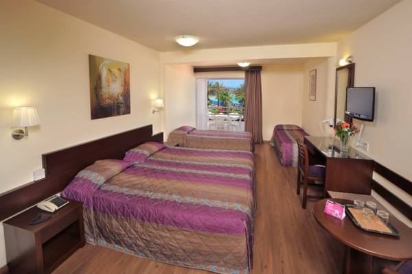 Ein Zimmer im Okeanos Beach Hotel mit drei Betten, Schreibtisch und Fernseher.