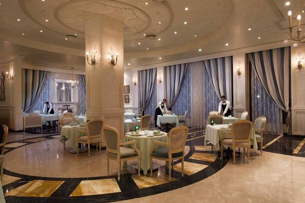 Innenansicht des Frühstücksrestaurants des Sunrise Arabian Beach Resort mit gedeckten Tischen, eleganten Stühlen und zwei Kellnern, die sich um die Tische kümmern.