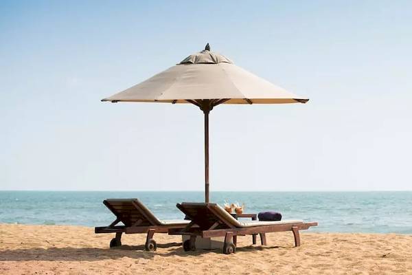 Zwei Liegen mit einem Sonnenschirm auf einem Strand vor dem Meer.