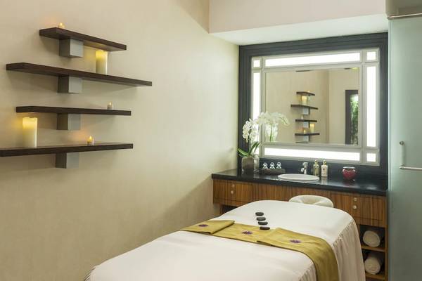 Spa-Behandlungsraum im Sheraton Oman mit Massageliege, Waschbecken und großen Spiegel.