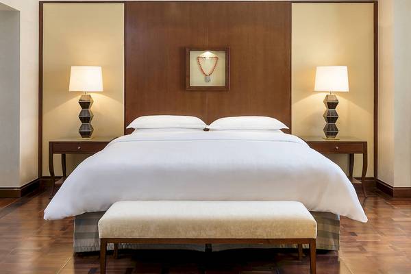 Schlafzimmer im Sheraton Oman Hotel mit luxuriöser Bettwäsche und dekorativer Halskette.