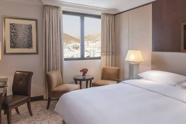 Ein elegantes Hotelzimmer im Sheraton Oman mit Blick auf die Stadt und Bergen.