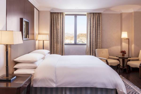 Hotelzimmer des Sheraton Oman mit Bett, Lampen und Blick auf die Stadt