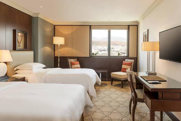 Doppelzimmer im Sheraton Oman Hotel mit zwei Betten, Schreibtisch und Panoramafenster.