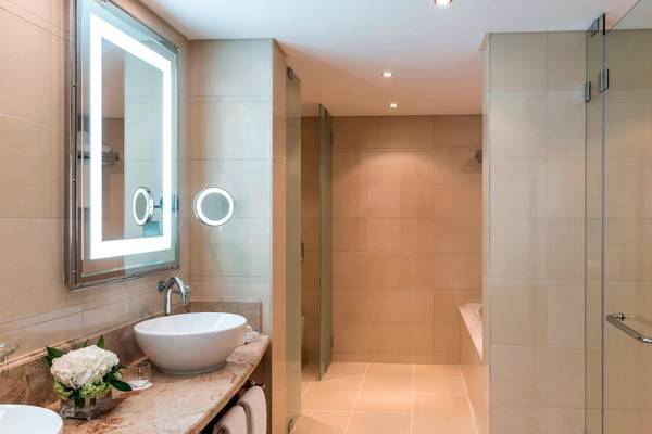 Badezimmer des Sheraton Oman Hotels mit einem Waschbecken, Spiegel und Dusche.