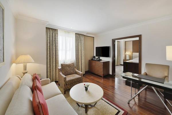 Innenansicht des Wohnzimmers im Sheraton Oman Hotel mit Fernseher, Tisch, Stühlen und Lampen.