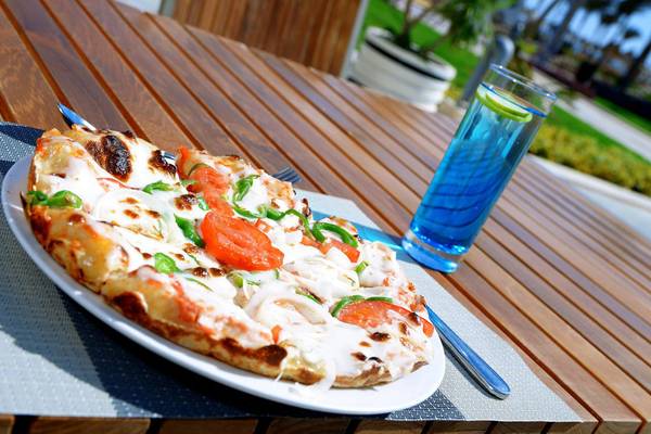 Eine Pizza auf einem Holztisch mit einem Glas blauem Getränk.