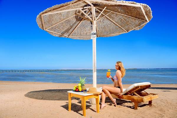 Eine Frau sitzt unter einem Sonnenschirm am Strand und genießt ein Getränk und Obst.