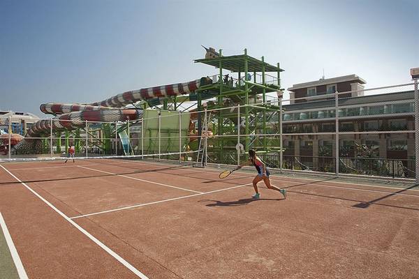 Tennisplatz im Crystal Waterworld Aqua Collection Hotel mit großer Wasserrutsche im Hintergrund.