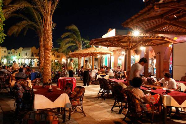 Das Sultan Bey Resort zeigt einen belebten Außenbereich des Restaurants bei Nacht mit vielen Gästen, die an Tischen sitzen.