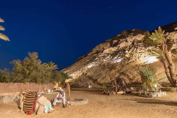 Sultan Bey Resort bei Nacht mit einem Mann, der neben einem Kamel auf einem Felsen sitzt.