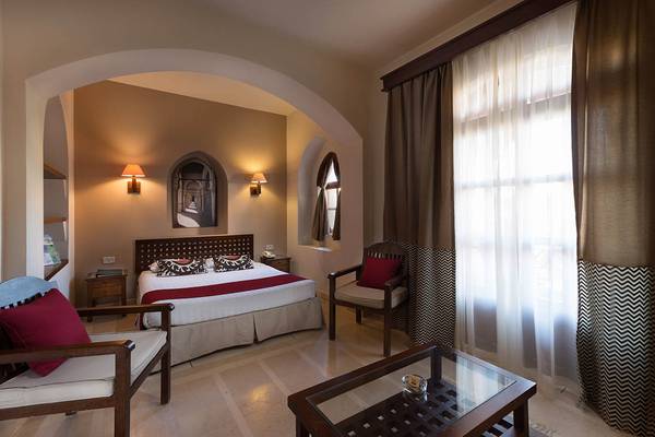 Innenansicht eines Hotelzimmers im Sultan Bey Resort mit einem Bett, Sesseln und einem Glastisch.