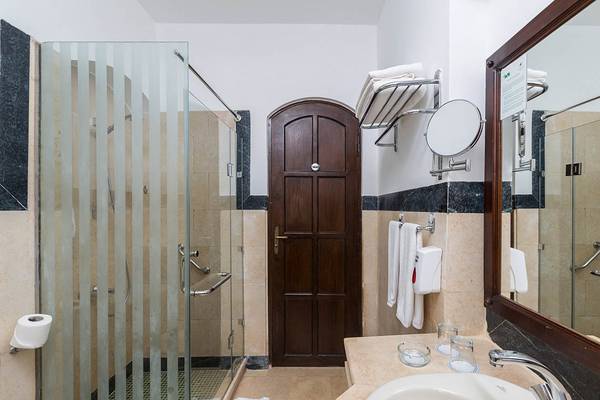 Badezimmer im Sultan Bey Resort mit Glasdusche, Holztür, Waschbecken und Spiegel.